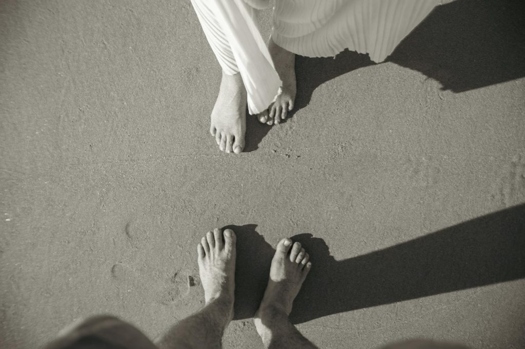 Artistic black and white image of a couple's feet on a sandy beach, capturing a romantic moment.