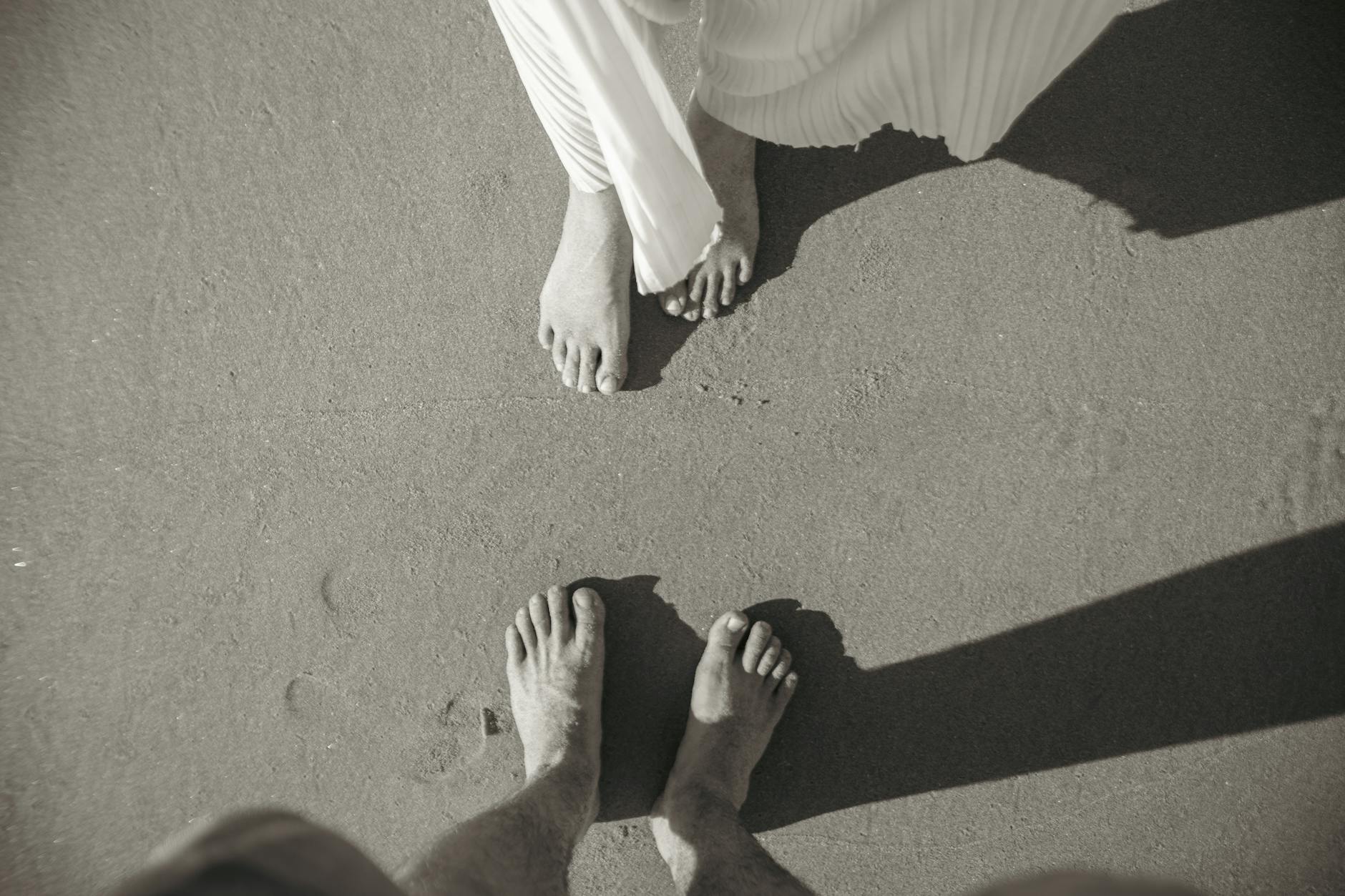 Artistic black and white image of a couple's feet on a sandy beach, capturing a romantic moment.